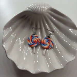 Örhängen-klubba💕💞 - Säljer ett par unika örhängen formade som klubbor i regnbågens färger. De har en spiraldesign med färger som röd, blå, gul och rosa. Perfekta för att ge en lekfull touch till din outfit!