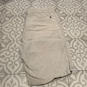 Beige linnebyxor från NN.07 - Snygga beige linnebyxor från NN.07 med dragkedja och knapp framtill. Perfekta för en stilren look med sina raka ben och klassiska design. Byxorna har hällor för bälte och är tillverkade i ett lätt och luftigt material. Nypris: 800kr