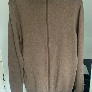 Brun kofta från Selected Homme - Säljer en stilren brun kofta från Selected Homme. Koftan har en dragkedja framtill och är tillverkad i ett mjukt material. Perfekt för lager-på-lager under kyligare dagar.