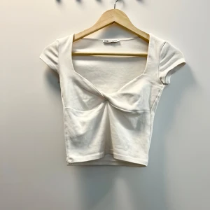 Topp - Vit, kortärmad topp från Zara med en unik detalj framtill. Toppen har en fyrkantig halsringning som ger en modern touch. Storlek S, passar oxå XS. I fint skick.🌸