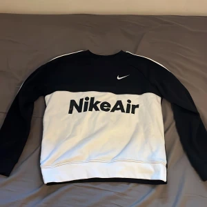 Svart och vit tröja från Nike - Säljer en snygg svart och vit tröja från Nike med texten 'Nike Air' på framsidan. Tröjan har långa ärmar och en klassisk design med vita detaljer längs ärmarna. Perfekt för en sportig look!
