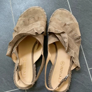 Bruna skinn  sandaler med volang och nitar - Snygga bruna sandaler från Cream med volangdetaljer och små nitar. Perfekta för sommardagar med en öppen tå-design och bekväm passform. Färgen är inte riktigt brun , mullvad . Mjuk mocka skinn 