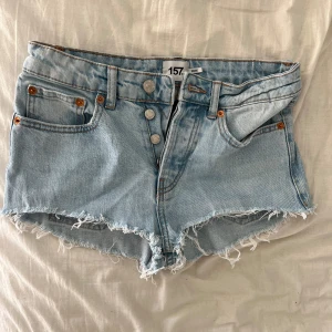 Lågmidjade Ljusblå jeansshorts med fransar - Säljer ett par ljusblå lågmidjade jeansshorts med fransiga kanter och knappgylf. Shortsen har en klassisk femficksdesign och är perfekta för sommardagar. De är både snygga och bekväma, ett måste i garderoben! Pris kan diskuteras🤗