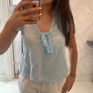  Ljusblå blus med knyt från Vera Moda! - Söt ljusblå blus med korta ärmar och knyt framtill. Perfekt för varma dagar och ger en fräsch look. Blusen har en v-ringad design och är tillverkad i ett lätt material. Använt 1 gång!💓