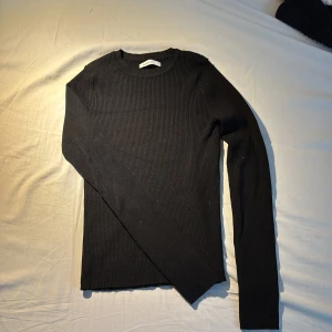 Svart ribbad tröja från Reserved - Säljer en stilren svart ribbad tröja från Reserved. Tröjan har en klassisk design med långa ärmar och rund halsringning. Perfekt för en enkel och snygg look.