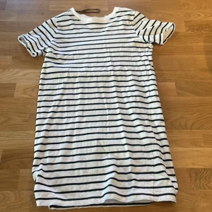 Randig klänning - Säljer en vit och svart randig klänning med korta ärmar. Perfekt för en avslappnad stil. Klänningen har en enkel och klassisk design som passar till många tillfällen.