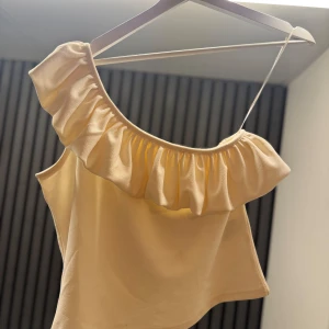 Beige offshoulder topp med volang - Säljer en söt beige offshoulder topp med volangdetalj. Perfekt för varma sommardagar. Toppen har en smickrande passform och är tillverkad i ett mjukt material. Andra bilden är lånad då den inte passar mig, men samma tröja