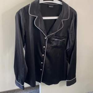 Svart pyjamassett med vita knappar  - Skönt pyjamassett i satin med både skjorta och byxorna ihop. Köpt på Gina tricot, jätte skönt o h fint material som är skönt att sova i. Priset går att diskutera💞