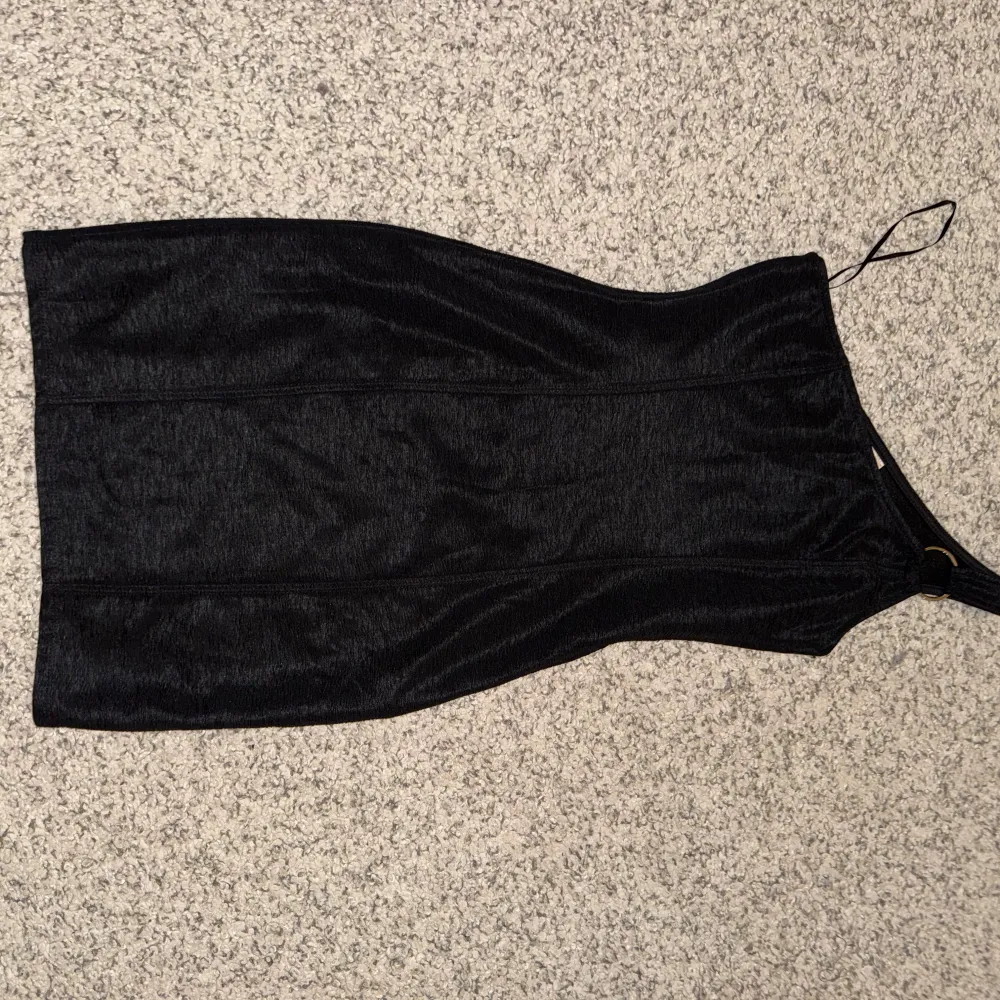 Snygg svart oneshoulder klänning med en elegant och stilren design. Perfekt för en kväll ute eller en speciell tillställning. Klänningen har en smickrande passform och är tillverkad i ett mjukt material. Har en silver detalj vid ärmen.. Mekot.