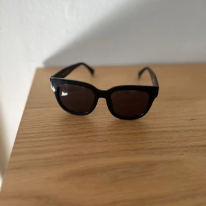 Corlin eyewear Svarta solglasögon - Snygga svarta solglasögon med rektangulära bågar. Perfekta för en stilren look och skyddar mot solen. Passar både till vardag och speciella tillfällen.