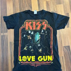 Svart KISS t-shirt från Gildan - Cool svart t-shirt från Gildan med KISS 'Love Gun' tryck i rött och gult. Perfekt för rockälskare som vill visa sin stil. Tillverkad i 100% bomull för en bekväm passform. Storlek S. Inte mycket använd. 