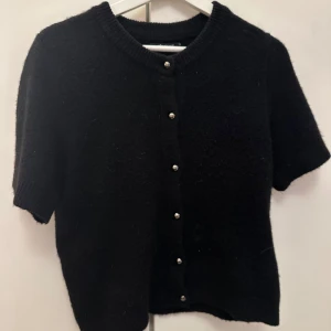 Svart kortärmad kofta med knappar - Säljer en stilren svart kofta med korta ärmar och silvriga knappar från Gina tricot. 