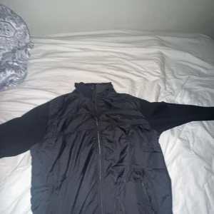 Svart väst med dragkedja från Lacoste  - Säljer en stilren svart väst med dragkedja. Perfekt för lager-på-lager och har en hög krage för extra skydd mot vind. Västen är enkel att matcha med olika outfits.