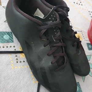 Fotbollsskor från Adidas i vitt och grönt - Säljer ett par snygga fotbollsskor från Adidas i vitt med gröna och svarta detaljer. Skorna har snörning och en sportig design som passar perfekt för fotbollsplanen.