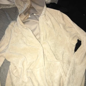Beige hoodie med dragkedja - Mysig beige hoodie med huva och dragkedja framtill. Tröjan har långa ärmar och en stor ficka på magen, perfekt för chill dagar. Tillverkad i mjukt material som känns skönt mot huden.