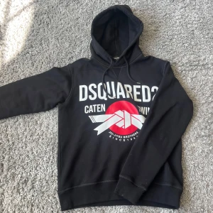 Svart hoodie från Dsquared2 med tryck - Svart hoodie från Dsquared2 med stort vitt och rött tryck framtill. Tröjan är i ny skick kom!! Finns kvitto! Byten är intressant.🙏🙏