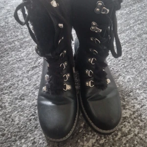 Svarta boots från Esprit med snörning - Snygga svarta boots från Esprit med grov snörning och pälsfoder på insidan. Skorna har rund tå, platt sula och detaljer i silvermetall. Yttermaterialet är i skinnimitation och insidan är fodrad för extra värme. Perfekta för kyliga dagar.