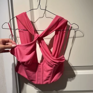 Rosa korsettopp från Zara - Säljer en snygg rosa korsettopp från Zara med breda axelband och twistad detalj framtill. Toppen har en croppad passform och är tillverkad i mjukt stretchigt material som sitter bekvämt. Perfekt för dig som vill sticka ut med en cool och trendig look.