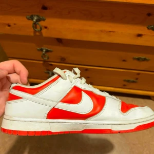 Nike Dunk Low röd/vit  - Nike Dunk Low sneakers i rött och vitt skinn. Klassisk siluett med vit swoosh, röda paneler och vit bas. Lågt skaft, snörning och perforerad tåbox för extra ventilation. Perfekta för dig som gillar retrovibbar och streetstyle.