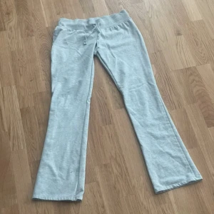 Ljusgrå low waist mjukisbyxor med snörning - Säljer ett par ljusgrå mjukisbyxor med bred resår i midjan och snörning framtill. Byxorna har en lätt utsvängd passform nertill och är tillverkade i mjukt bomullsmaterial. Perfekta för chill dagar eller när du vill vara bekväm men ändå se snygg ut.