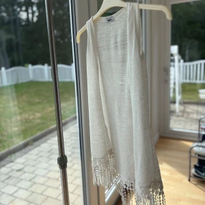 Vit ärmlös cardigan med fransar - Superfin vit ärmlös cardigan med snygga virkade fransdetaljer längst ner. Tunt och luftigt material som känns perfekt för varma dagar. 