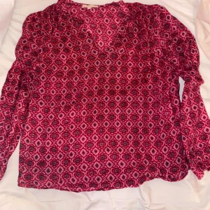 Blus - En jättefin röd blus med coolt mönster. Jättefin att klä upp sig men och passar till de flesta underdelar att matcha med. 