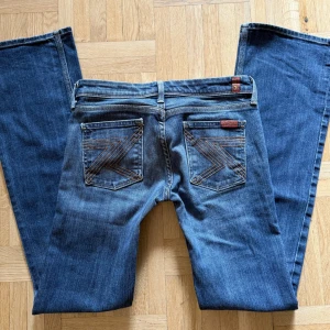 Blå bootcut jeans från 7 For All Mankind - Snygga blå jeans från 7 For All Mankind med klassisk bootcut-modell. Jeansen har låg midja och coola broderade bakfickor med bruna detaljer. Tillverkade i mjukt denimtyg som sitter skönt och ger en clean look.