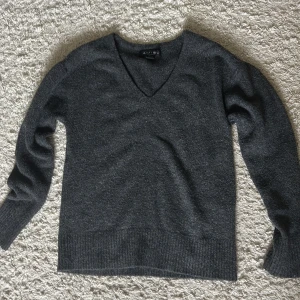 Mörkgrå v-ringad stickad tröja  - Mysig mörkgrå stickad tröja från New Yorker med v-ringning och långa ärmar. Tröjan har ribbade muddar vid ärmslut och nederkant, perfekt för lager på lager. Enkel och stilren design som funkar till det mesta.