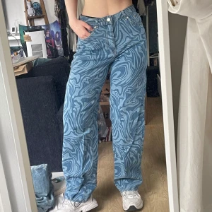 Blå swirlmönstrade baggy jeans, H&M Divided - Säljer ett par blå jeans med coolt swirlmönster. Byxorna har en loose/wide passform med raka ben, klassiska fem fickor och knappgylf. Perfekta för dig som vill sticka ut med coola mönster och bekväm stil. Passar baggy på en 36a, men passar även väl på en storlek 38. Aldrig använda, endast provade. 