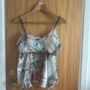 Mönstrad linnetopp från KappAhl - Säljer en luftig linnetopp från KappAhl med brunt, vitt och blått abstrakt mönster. Toppen har smala axelband, omlott vid bysten och dekorativa pärlor under bysten. Perfekt för varma dagar och ger en bohemisk vibe.💗