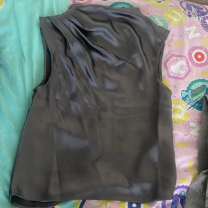 Grå satinblus från H&M XS - Snygg grå blus i satin från H&M i storlek XS. Ärmlös modell med lätt drapering vid axeln och diskret dragkedja i sidan. Perfekt för dig som gillar en stilren och elegant look med lite glansig finish.