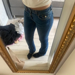 Blå bootcut jeans med låg midja - Snygga blå jeans med bootcut och låg midja. Jeansen har klassiska fickor fram och bak med coola detaljer och kontrastsömmar. Perfekt passform som sitter tajt upptill och släpper vid vaden. Tillverkade i mjukt denimtyg.