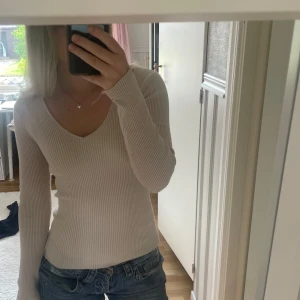 Beige ribbad långärmad tröja - Säljer en beige, ribbad långärmad tröja med v-ringning. Tröjan har en slim passform och är superenkel att matcha till olika outfits. Perfekt för dig som gillar en stilren och basic look. Strl M men sitter som en S