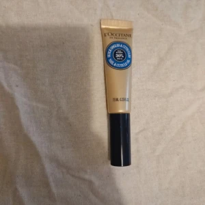 L'Occitane nagel- och nagelbandsolja - En smidig tub med nagel- och nagelbandsolja från L'Occitane, innehåller 7,5 ml och har en beige och svart design. Perfekt för att vårda torra nagelband och ge extra fukt med 30% sheasmör.