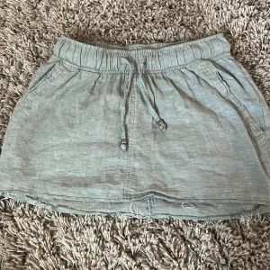 Ljusgrå kortkjol från Esmara - Superskön ljusgrå kortkjol från Esmara med resår i midjan och snörning med metallpärlor. Kjolen har råa kanter nertill för en chill vibe och är gjord i ett mjukt bomullsliknande material. Perfekt för varma dagar och enkel att matcha med allt.