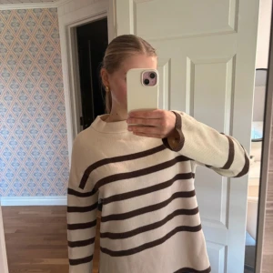 Randig beige tröja från Vero Moda - Säljer en beige långärmad tröja från Vero Moda med bruna ränder. Tröjan har en avslappnad passform och är tillverkad i mjukt stickat material. Perfekt för dig som gillar en enkel men snygg stil.