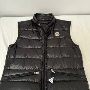 Moncler gui väst - Säljer en svart dunväst från Moncler väldigt skön och snygg. Perfekt att slänga över en hoodie eller tröja när det är kyligt ute.