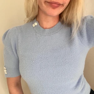 Ljusblå stickad tröja från Zara - Superfin ljusblå stickad tröja från Zara med korta ärmar och puff vid axlarna. Tröjan har glittriga pärlknappar vid halsen och på ärmarna som ger en extra touch. Mjuk och mysig, perfekt för att lyfta din outfit. Finns ingen prislapp kvar, men har aldrig använt den!