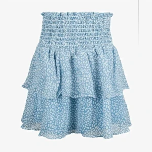 Blå volangkjol med leopardmönster - Supersöt blå kortkjol med vita leopardfläckar och volanger. Kjolen har smock i midjan för en bekväm passform och är perfekt för dig som gillar en lekfull och trendig stil.