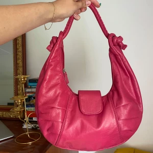 Rosa axelväska☀️☀️ - Säljer en snygg rosa axelväska i fuskskinn med rundad form och coola knutdetaljer på axelbandet. Väskan har ett lock framtill och dragkedja på insidan. Perfekt storlek för mobilen, plånboken och lite till. En riktig färgklick till din outfit!❤️ Använt men fint skick!