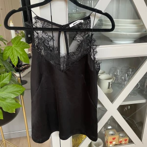 Svart spetslinne från Gina Tricot - Supersnygg svart linnetopp från Gina Tricot med v-ringning och bred spetskant upptill. Axelbandslös känsla med transparent mesh och spetsdetaljer som ger en lyxig vibe. Perfekt att styla med jeans eller kjol för en trendig look.