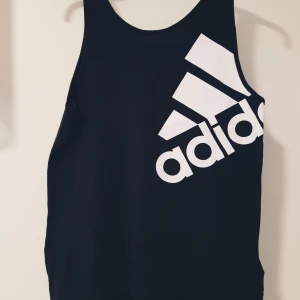 Svart linnetopp från Adidas XS - Sportig svart linnetopp från Adidas med stort vitt logotryck över bröstet. Tillverkad i lätt och svalt climalite-material som andas, perfekt för träning eller gym. Klassisk rak passform och ärmlös design för maximal rörelsefrihet.  Helt skick dock små obehandlade fläckar på trycket & små tvättludd
