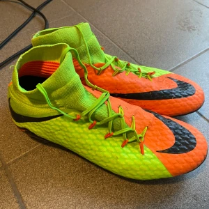 Nike Hypervenom fotbollsskor neon/orange - Säljer ett par Nike Hypervenom fotbollsskor i neon-grönt och orange med svarta detaljer och stora Nike-loggor. Skorna har snörning, hög strumpliknande krage och dobbar för gräsplan.                                                                  Sällsynt äldre modell av Nike Hypervenom (säljs inte längre) Storlek: 44 - 44,5  Använda sparsamt och inga defekter  Skick: 8,5/10 Pris: 500 Skriv gärna vid frågor! Pris kan diskuteras!