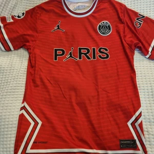 PSG Messi #30 röd matchtröja Nike - Röd Paris Saint-Germain fotbollströja med Messi #30 på ryggen. Tröjan har korta ärmar, svarta och vita detaljer, PSG-emblem och Jordan-logga på bröstet. 