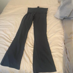 Mörkgrå bootcut yogapants  - Snygga mörkgrå yoga pantsmed bootcut från Gina Tricot. Byxorna är i mjukt material och har en bred linning upptill som ger en skön och avslappnad look. Perfekta för chill dagar eller när du vill vara bekväm men ändå se trendig ut.