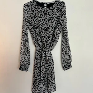 Svartvit leopardmönstrad klänning - Snygg svartvit klänning med leopardmönster och lång ärm. Modellen är kort och har knyt i midjan som gör att klänningen sitter fint mot kroppen. Väldigt luftig klänning. 
