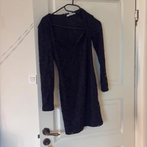 Svart spetsklänning från nelly  - Supersnygg svart kort spetsklänning från nelly med lång ärm och figurnära passform. Klänningen har v-ringad urringning och dragkedja i ryggen. Prrfekt för klubbeeen län.