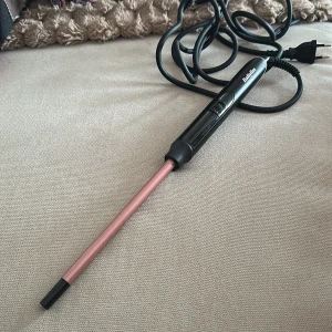 BaByliss locktång med smal stav - Säljer en BaByliss locktång med smal, rosa stav och svart handtag. Perfekt för att skapa tighta lockar eller beach waves. Utrustad med enkla reglage på handtaget och lång sladd för smidig styling. Modell C449E, 25W.