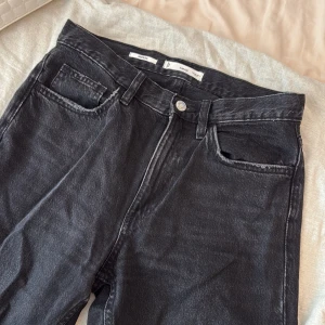 Svarta raka jeans från Mango - Snygga svarta jeans från Mango med raka ben och klassisk femficksdesign. Jeansen har hög midja och är tillverkade i ett robust bomullstyg med lätt tvättad look. Perfekta för dig som gillar en enkel och stilren vibe.