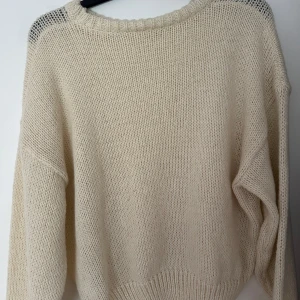 Beige stickad tröja - Mysig beige/offwhite stickad tröja med avslappnad oversized passform. Tröjan har rund halsringning och långa ärmar, perfekt för lager på lager under kyliga dagar. Enkel och stilren design som passar till allt.